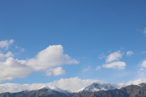 A wide shot of a mountain range under a clear blue sky with fluffy white clouds.