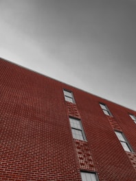 A brick building with geometric patterns in the masonry, featuring several windows. The sky is overcast and appears gray, creating a stark contrast with the rich red tones of the bricks.