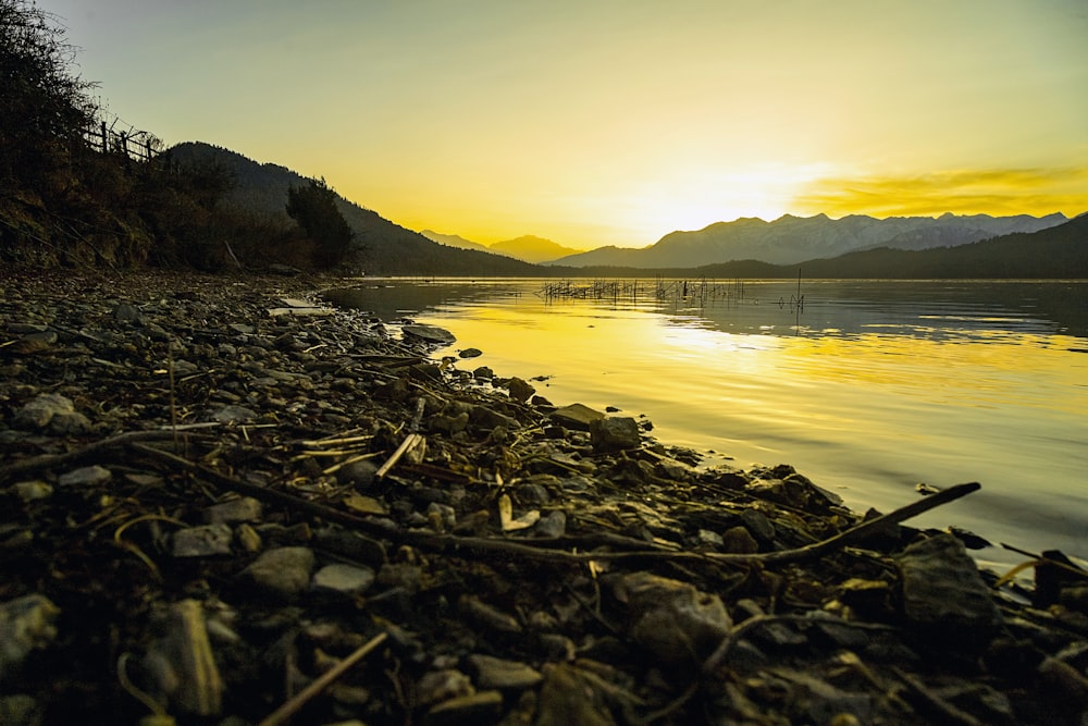 the sun is setting over the water and rocks