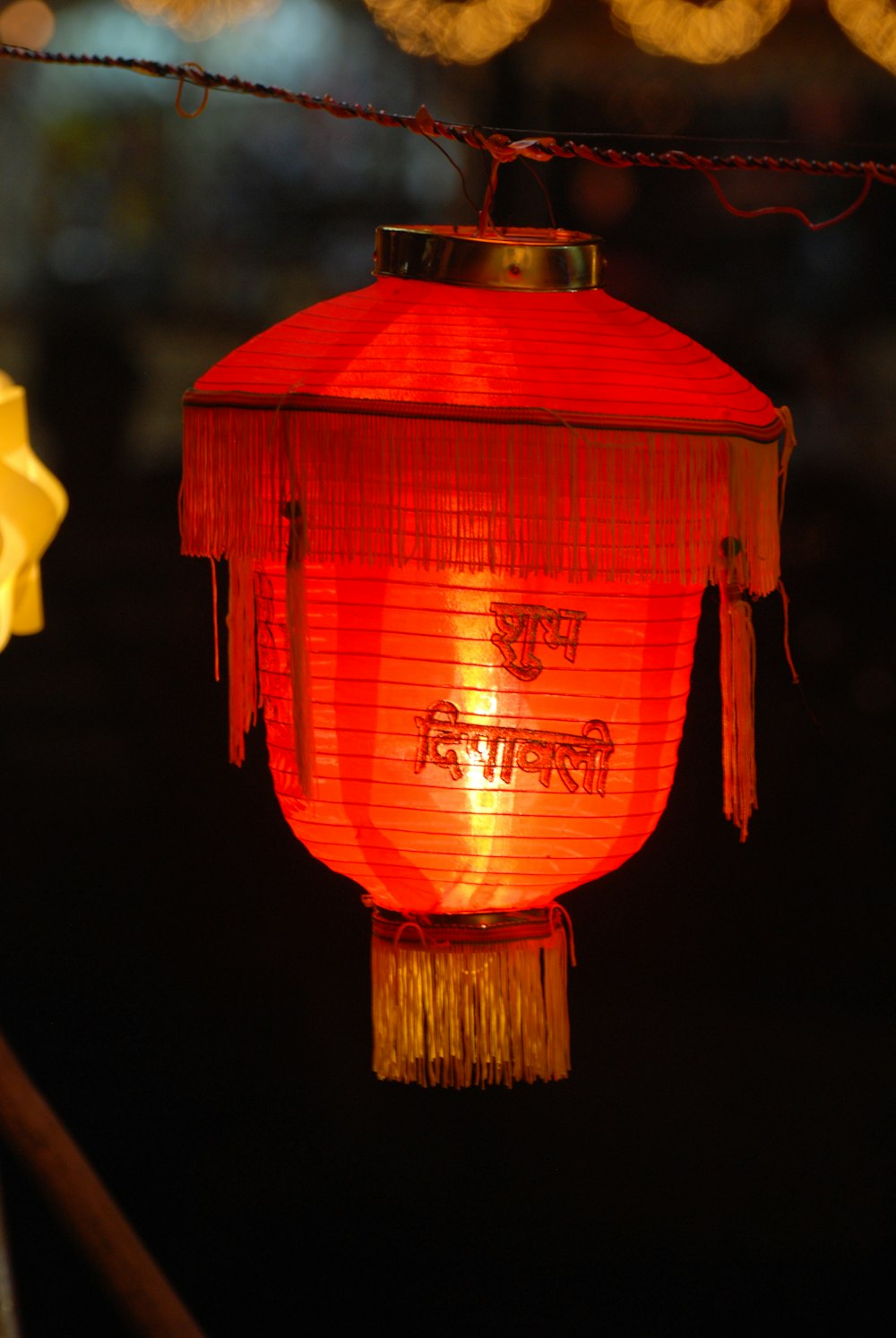 a red lantern hanging from a wire with lights in the background