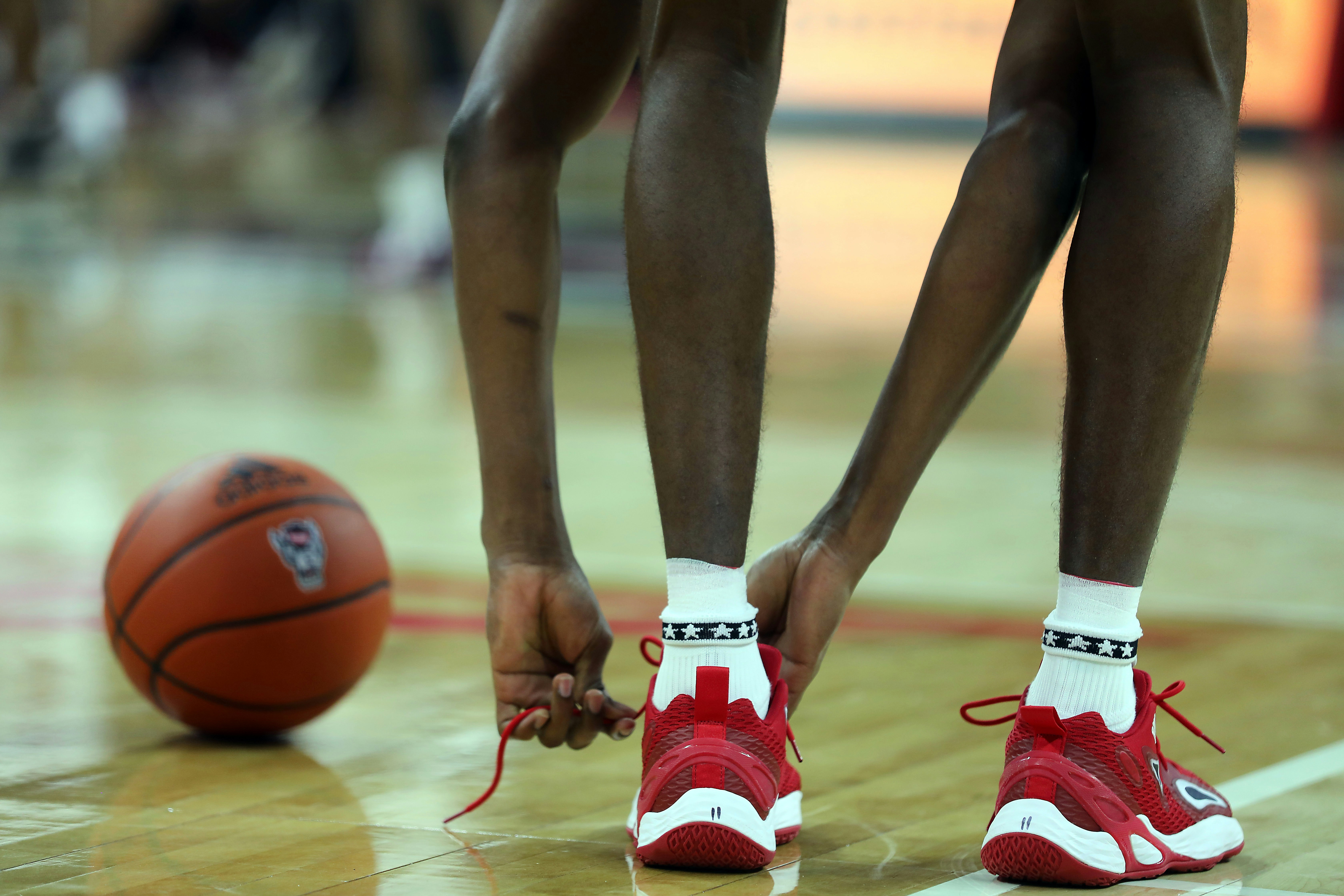 NC State basketball player ties shoelaces on sneakers during basketball game at PNC Arena in Raleigh, North Carolina.