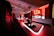 A modern gaming setup featuring several high-end computers with illuminated red interior lighting. The room is equipped with gaming chairs exhibiting a sleek black and red design. Multiple monitors are arranged on a long desk, and peripheral devices like keyboards and mice are uniformly placed, reflecting an ambiance ideal for gaming or competitive play.