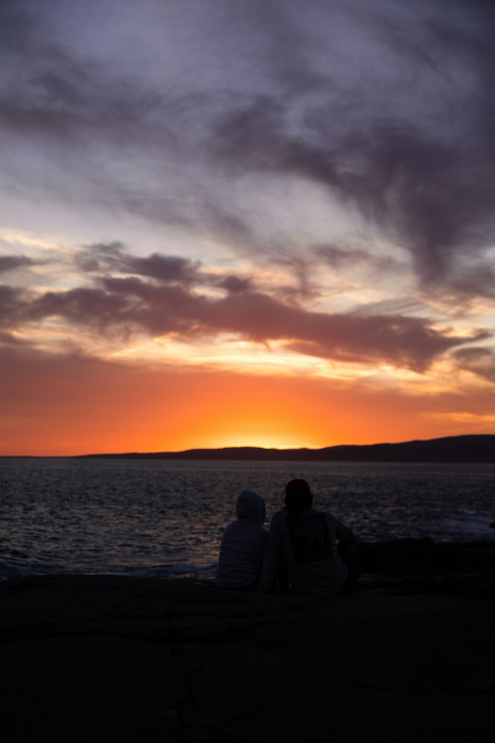two people sitting on a bench watching the sunset