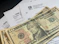 Several U.S. ten-dollar bills are placed on top of IRS tax forms and documents, including Form 1040 and envelopes addressed from the Department of the Treasury and Internal Revenue Service.