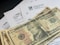 Several U.S. ten-dollar bills are placed on top of IRS tax forms and documents, including Form 1040 and envelopes addressed from the Department of the Treasury and Internal Revenue Service.