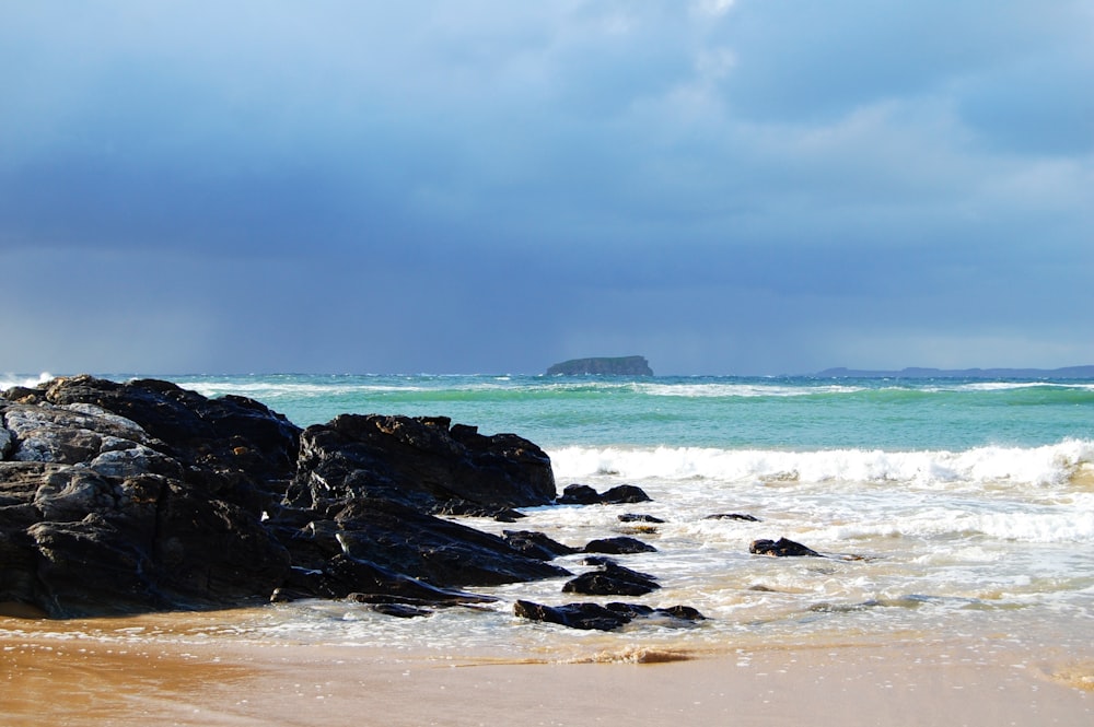 a beach with rocks and water under a cloudy sky