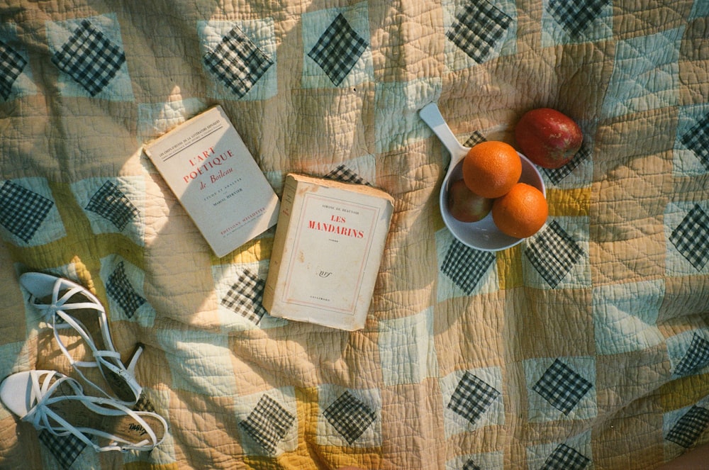 a table topped with books and fruit on top of a blanket