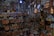 A collection of handcrafted metal items, predominantly copper and brass, displayed on shelves and hanging from the ceiling. The assortment includes trays, pots, and pitchers, featuring intricate designs and patterns. The setting has a warm, vintage feel, with ambient lighting enhancing the metallic sheen.