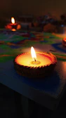 Festive scene showing multiple diyas lit on a wooden tray, surrounded by colorful rangoli and maroon and gold decorative borders.
