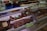 A display of various cuts of cured meat in a butcher shop, including different sizes and shapes of dark brown and reddish-brown meats, some of which are labeled with prices. The meats are placed inside a refrigerated glass case and there are trays and tools visible in the background.