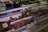 A display of various cuts of cured meat in a butcher shop, including different sizes and shapes of dark brown and reddish-brown meats, some of which are labeled with prices. The meats are placed inside a refrigerated glass case and there are trays and tools visible in the background.