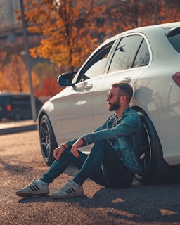 a man sitting on the ground next to a white car