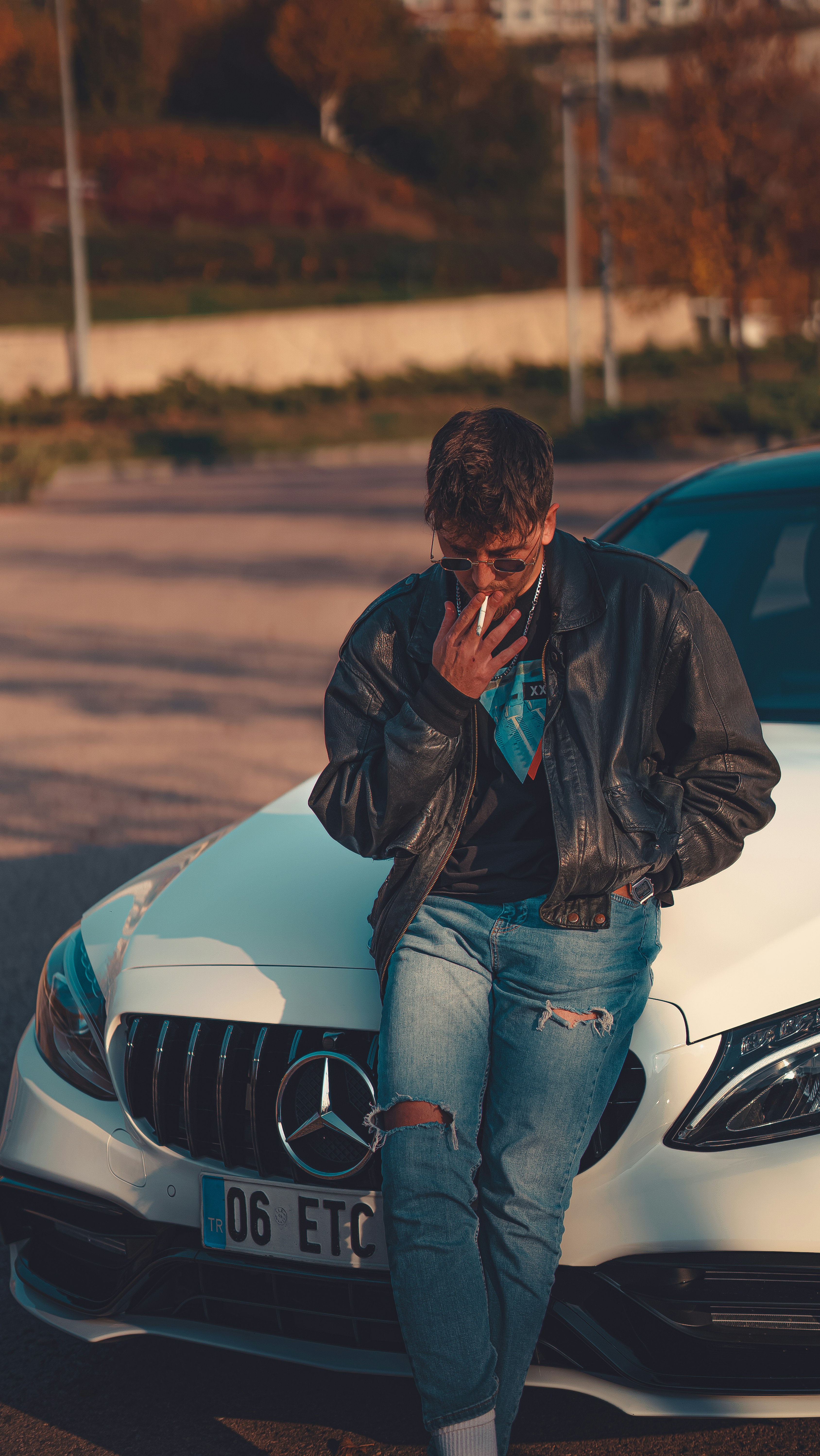 a man sitting on a car talking on a cell phone