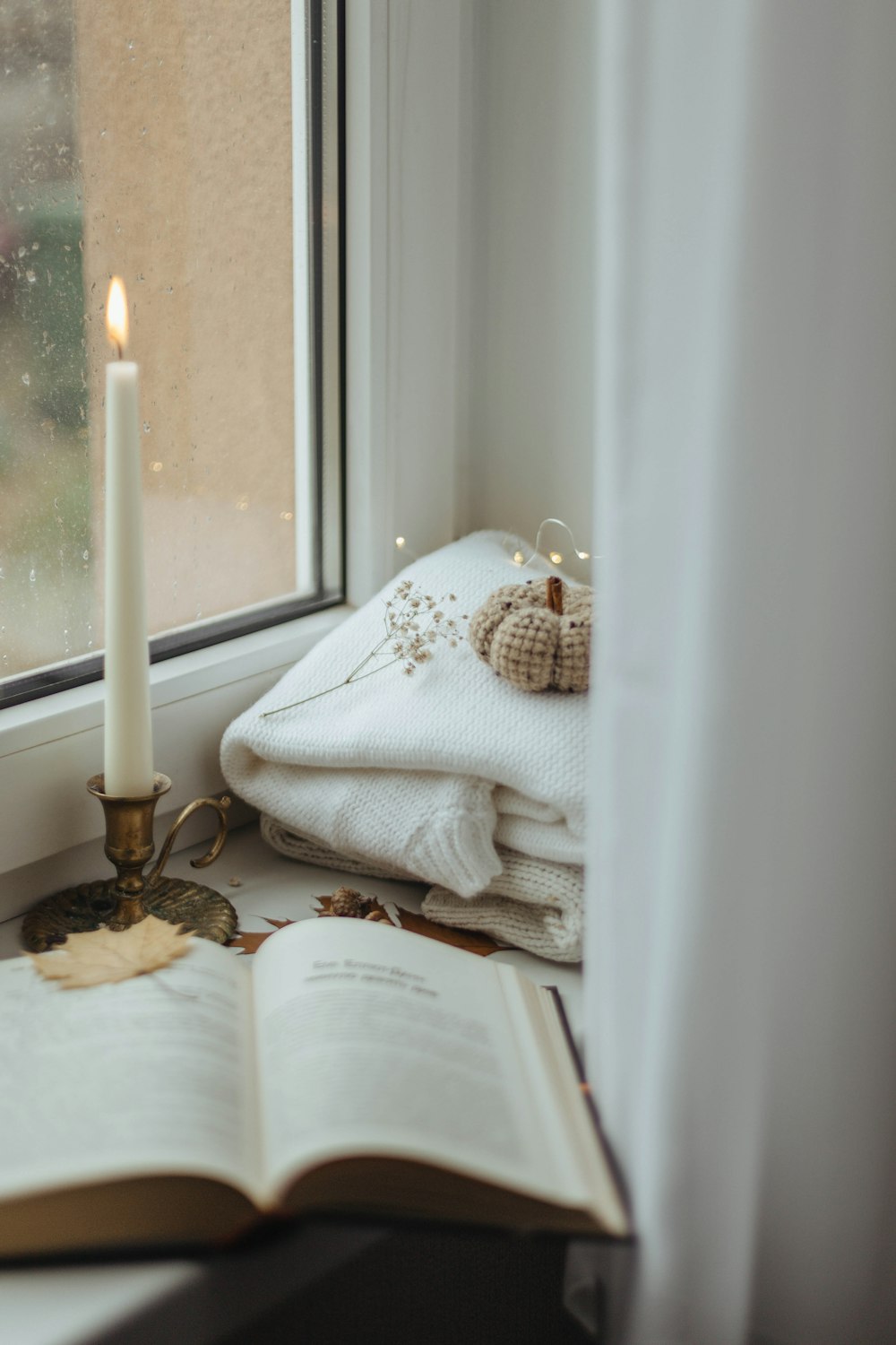 an open book sitting on a window sill next to a candle
