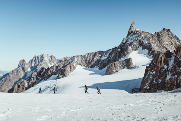 A group of skiers crossing a wide snowfield beneath jagged granite spires