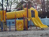 a playground with a yellow slide and a blue fence
