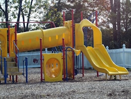 a playground with a yellow slide and a blue fence
