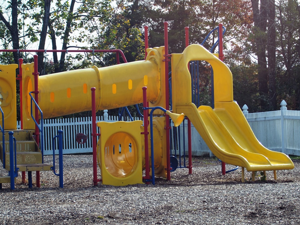 a playground with a yellow slide and a blue fence
