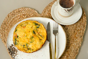 a white plate topped with a quiche next to a cup of coffee