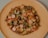 A homemade pizza topped with sliced mushrooms, sausages, bell peppers, and melted cheese is placed on a light wooden plate against a neutral background.