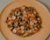A homemade pizza topped with sliced mushrooms, sausages, bell peppers, and melted cheese is placed on a light wooden plate against a neutral background.