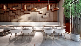 A modern, stylish interior with wooden walls featuring geometric patterns and warm lighting. The space includes sleek tables and chairs with light-colored upholstery, complemented by a potted green plant in the corner. The design is minimalistic yet inviting.