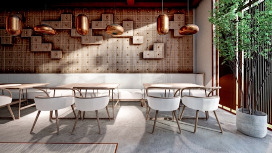 A modern, stylish interior with wooden walls featuring geometric patterns and warm lighting. The space includes sleek tables and chairs with light-colored upholstery, complemented by a potted green plant in the corner. The design is minimalistic yet inviting.
