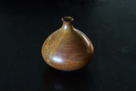 Close-up of a beautifully glazed ceramic vase with earthy tones on a wooden table