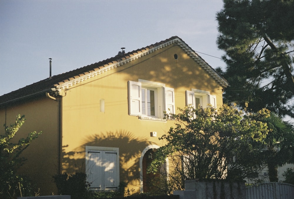 una casa amarilla con persianas blancas y un árbol frente a ella