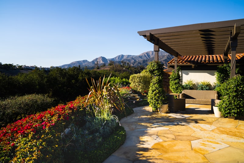 a covered patio with a bench and flowers in the foreground