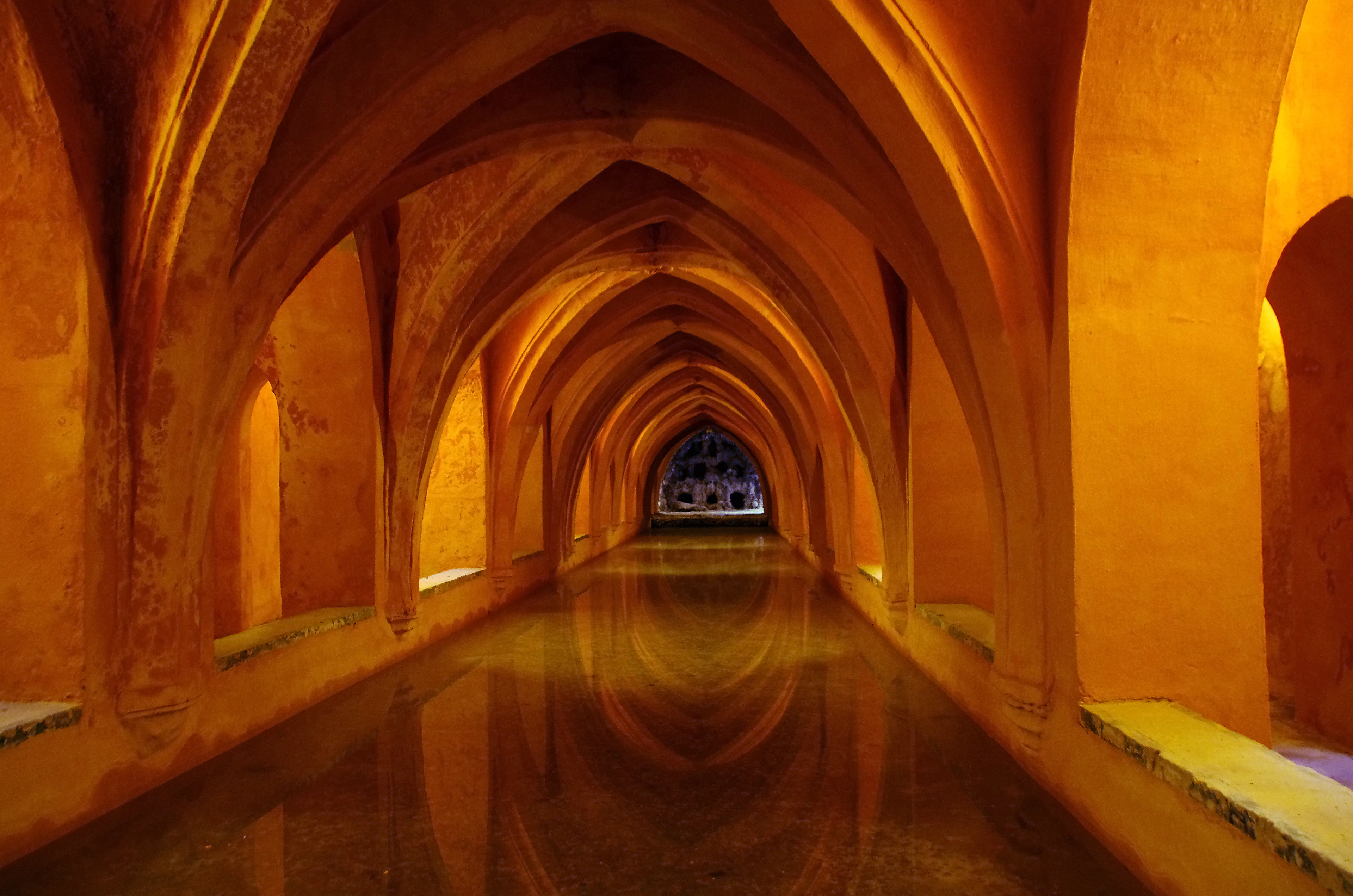 The vaulted underground Baths of Dona Maria de Padilla in Seville's Real Alcazar, its ochre arches mirrored in the still water