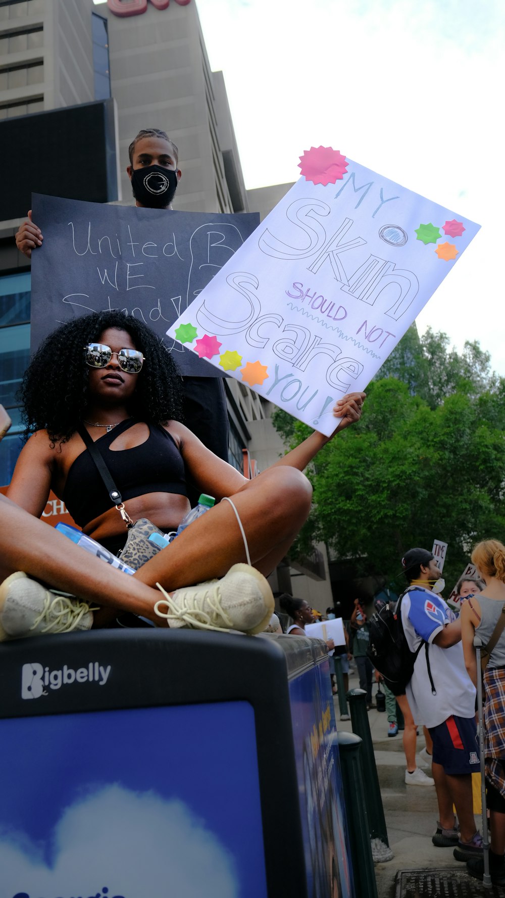 a woman sitting on top of a blue box holding a sign