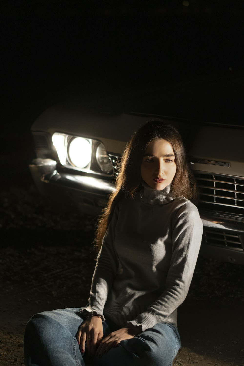 a woman sitting on the ground in front of a car