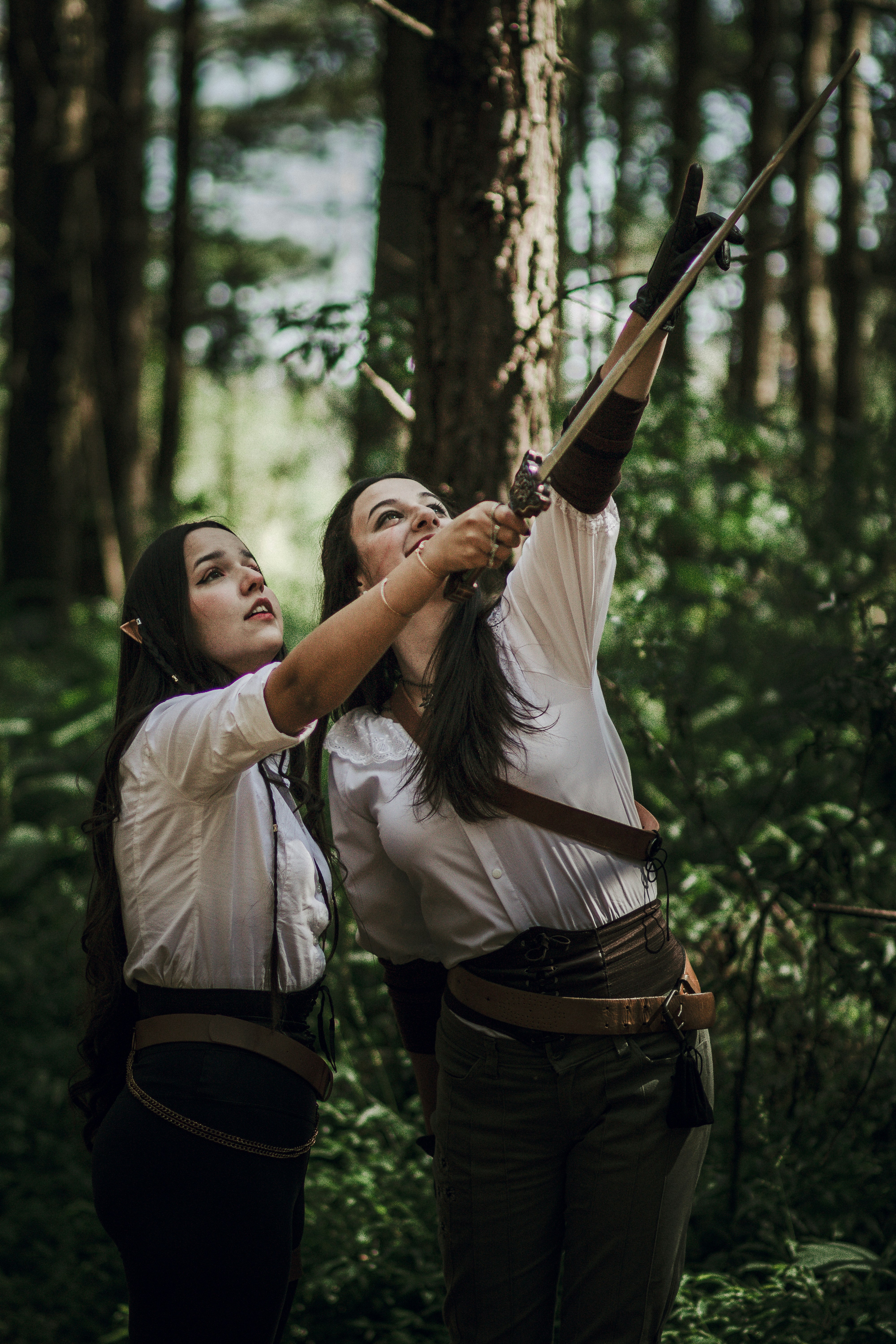 two women in the woods with a bow and arrow