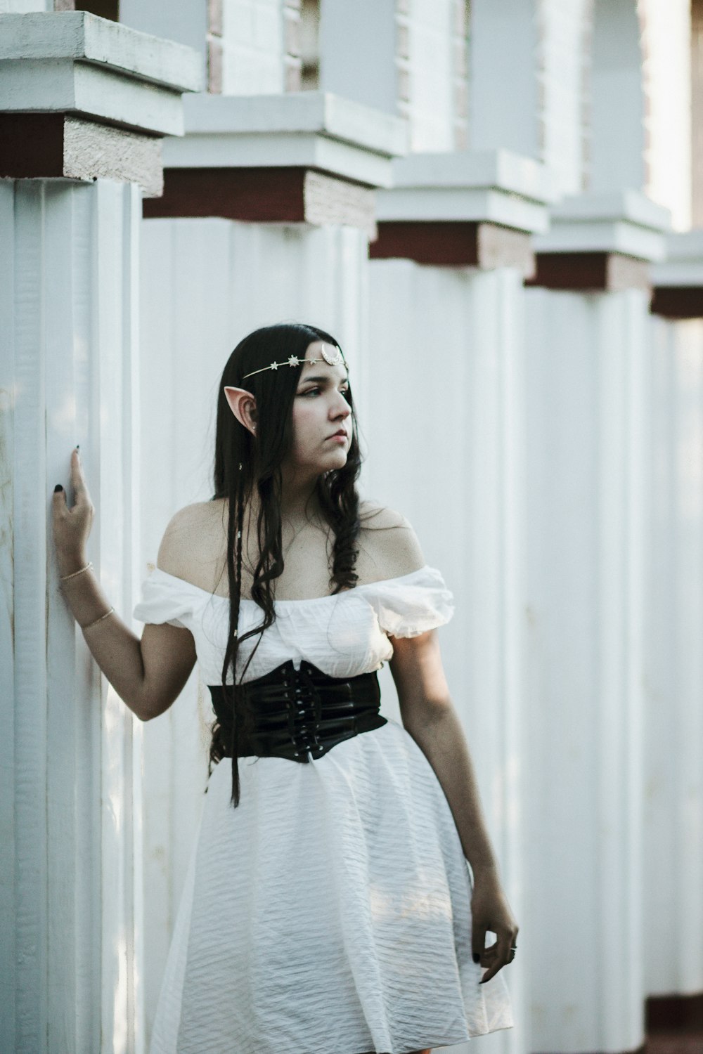 a woman in a white dress is leaning against a wall