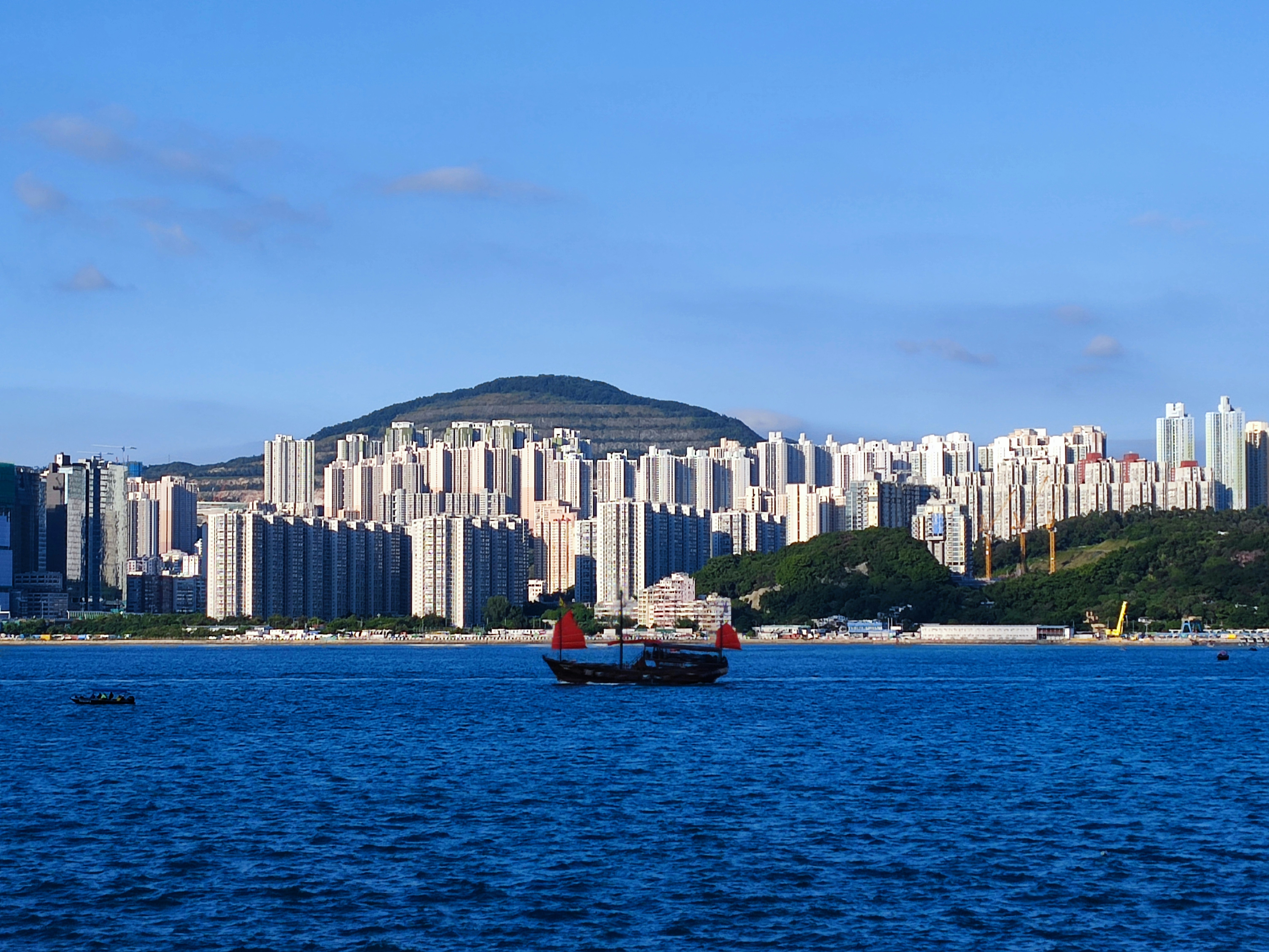 Laguna City on the left and Cha Kwo Ling (Ling means a range of hills) on the right, which comprise a section of the coastline in Lam Tin District, Eastern Kowloon Peninsula, Hong Kong. The photo was taken from the opposite side of Victoria Harbour at the promenade of Quarry Bay Park on Hong Kong Island. The quarry on the hilltop is Anderson Road Quarry which is now converted into new residential developments. The Chinese junk boat floating pass is Aqua Luna(張保仔號）, a tourist attraction to enjoy a boat ride in the Victoria Harbour day and night to see the Pearl of the Orient.