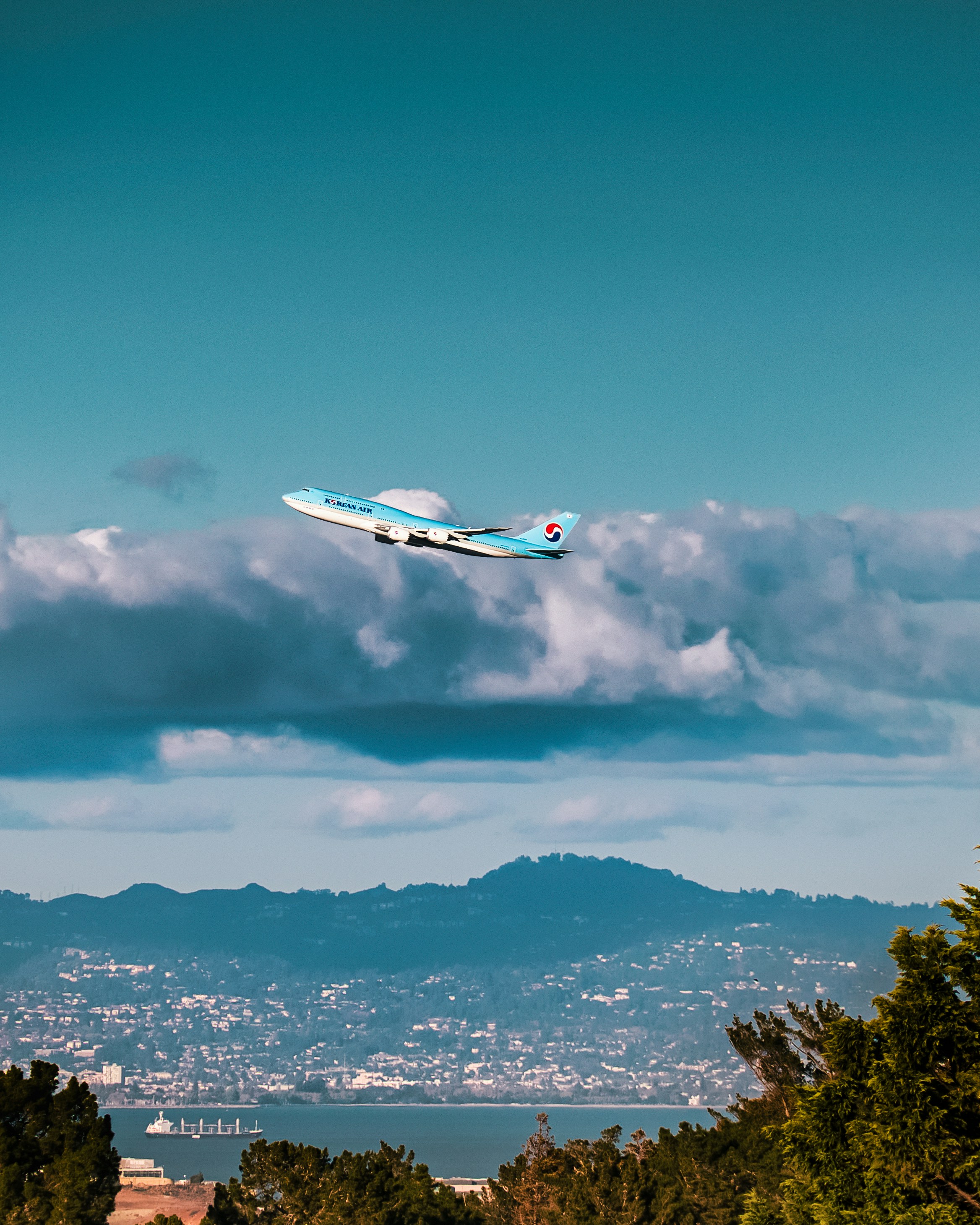 산을 배경으로 도시 위를 비행하는 비행기