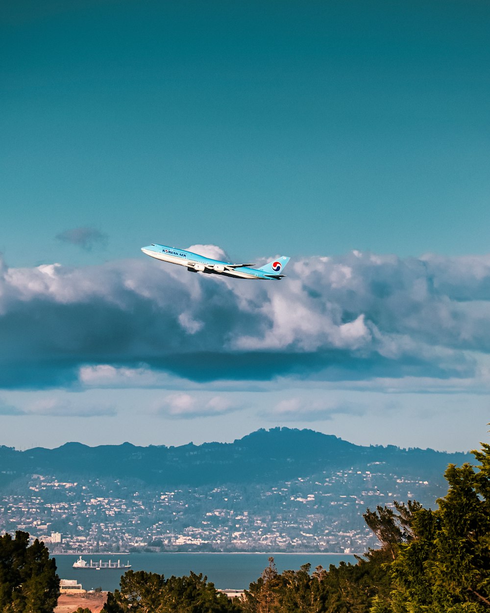a plane flying over a city with mountains in the background