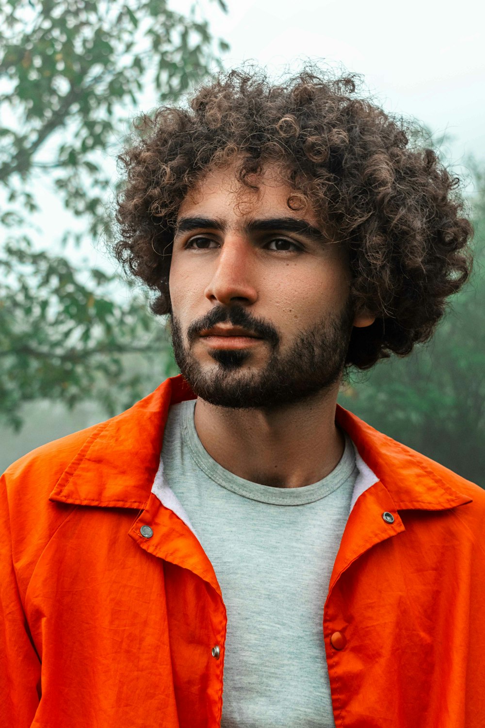 a man with curly hair wearing an orange jacket
