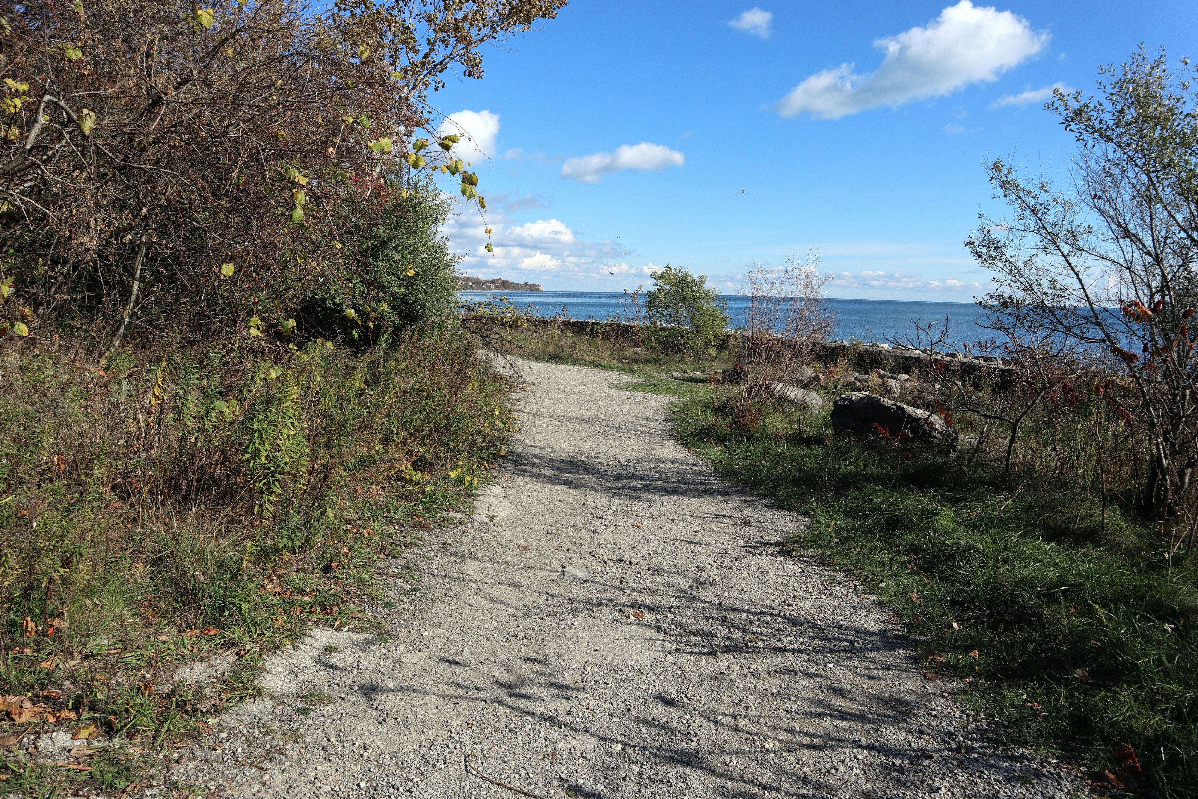 a dirt road next to a body of water, The paved trail will soon come to end as we head east towards the coastline. 