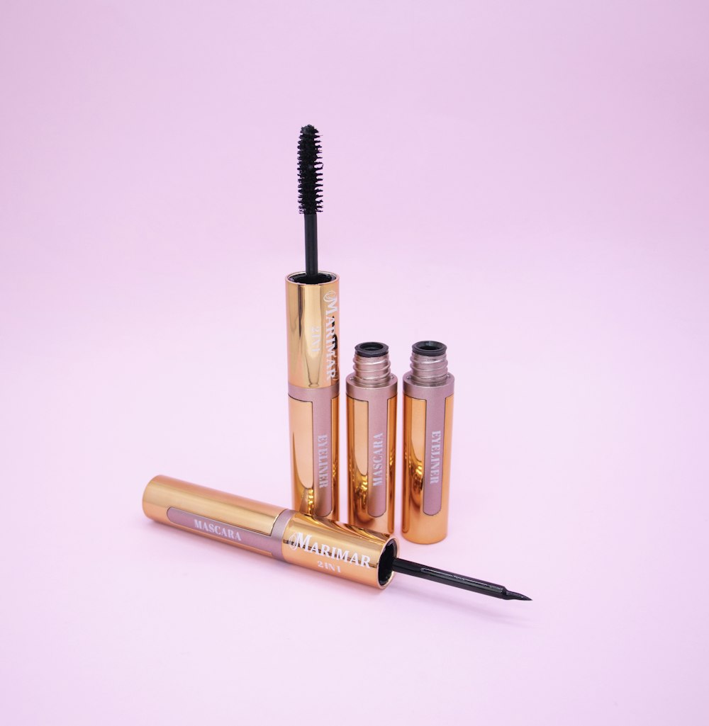 three mascaras and a brush on a pink background