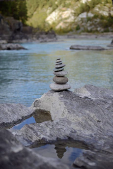 A serene stack of smooth stones balanced gently on a sandy surface with a delicate green leaf resting nearby.