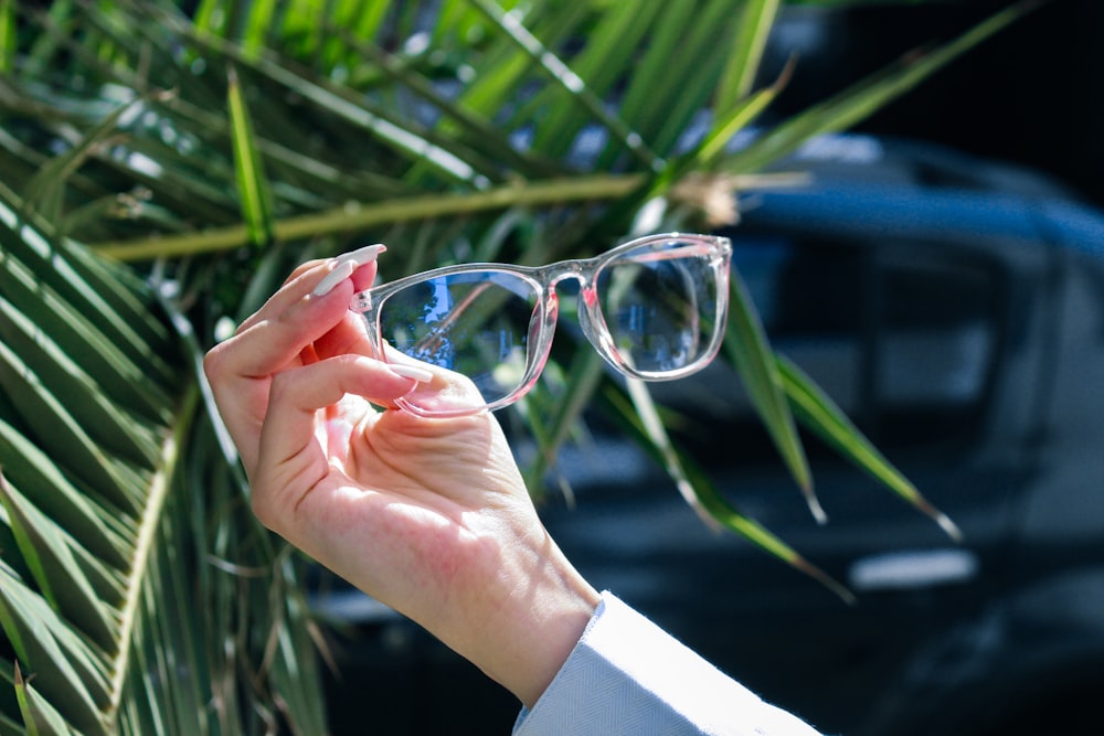 a woman holding up a pair of glasses in front of a palm tree