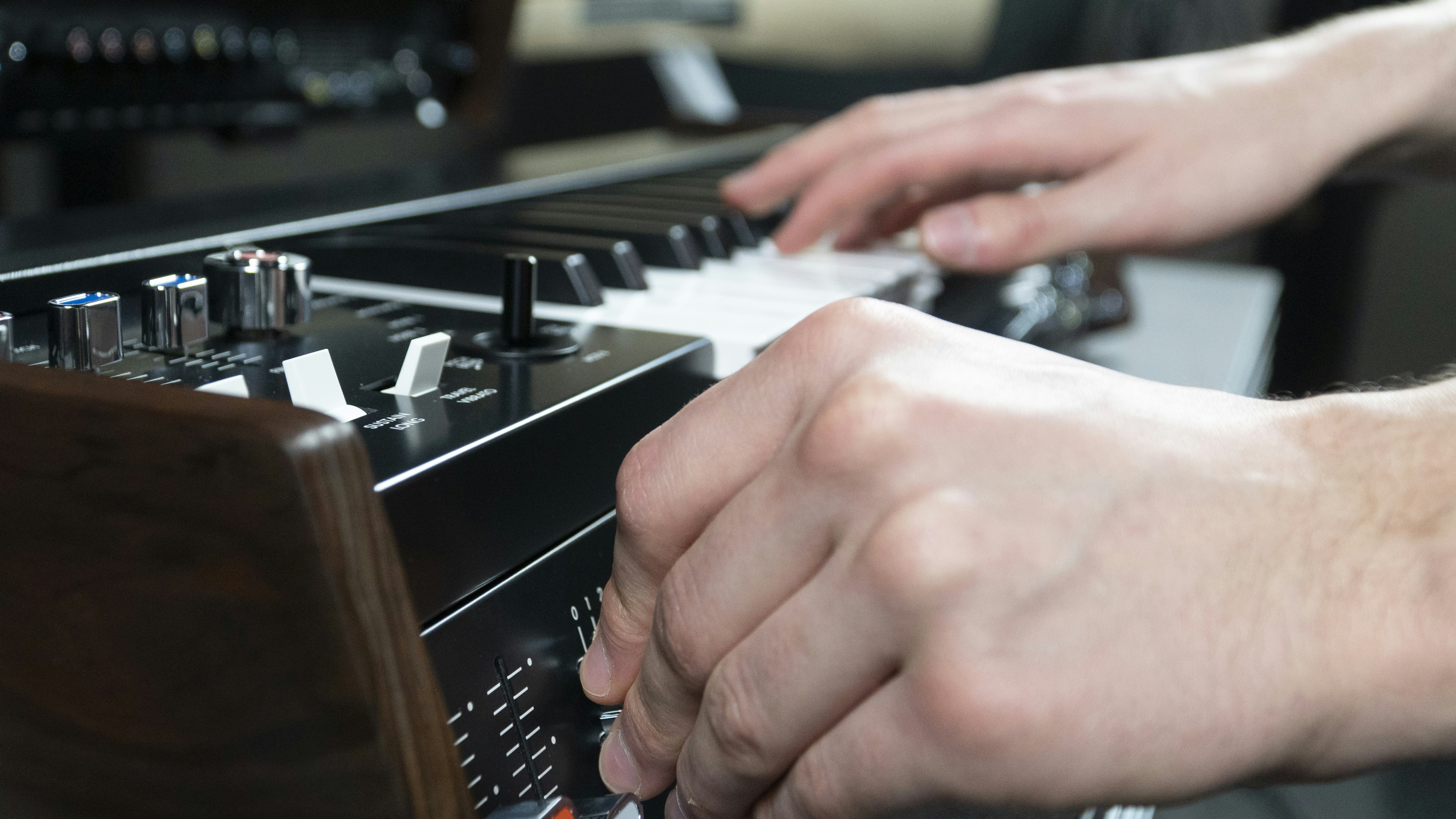 Hands play keys and turn a knob on a synthesizer.