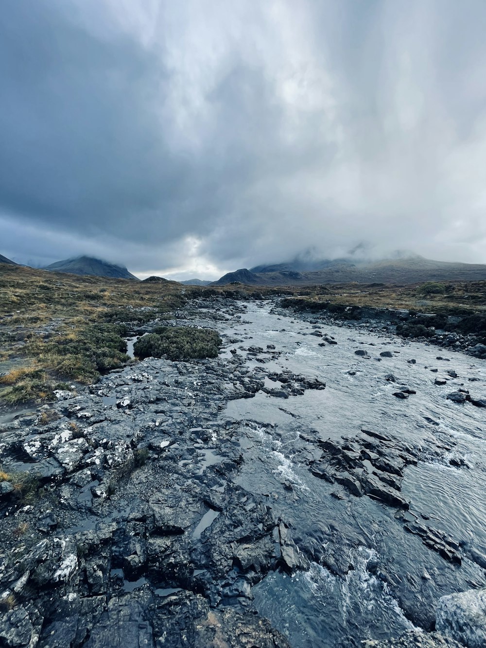 a river running through a lush green field under a cloudy sky