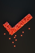 An arrangement of numerous small red crosses forms a large checkmark shape against a dark background, with several individual crosses scattered below.