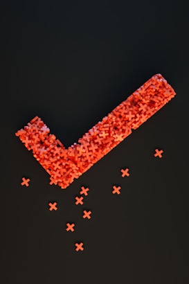 An arrangement of numerous small red crosses forms a large checkmark shape against a dark background, with several individual crosses scattered below.