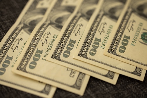 Stacks of US one hundred dollar bills laid out in a slightly fanned arrangement on a dark surface.