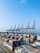 A busy cargo port with containers being loaded onto a ship under a clear blue sky.