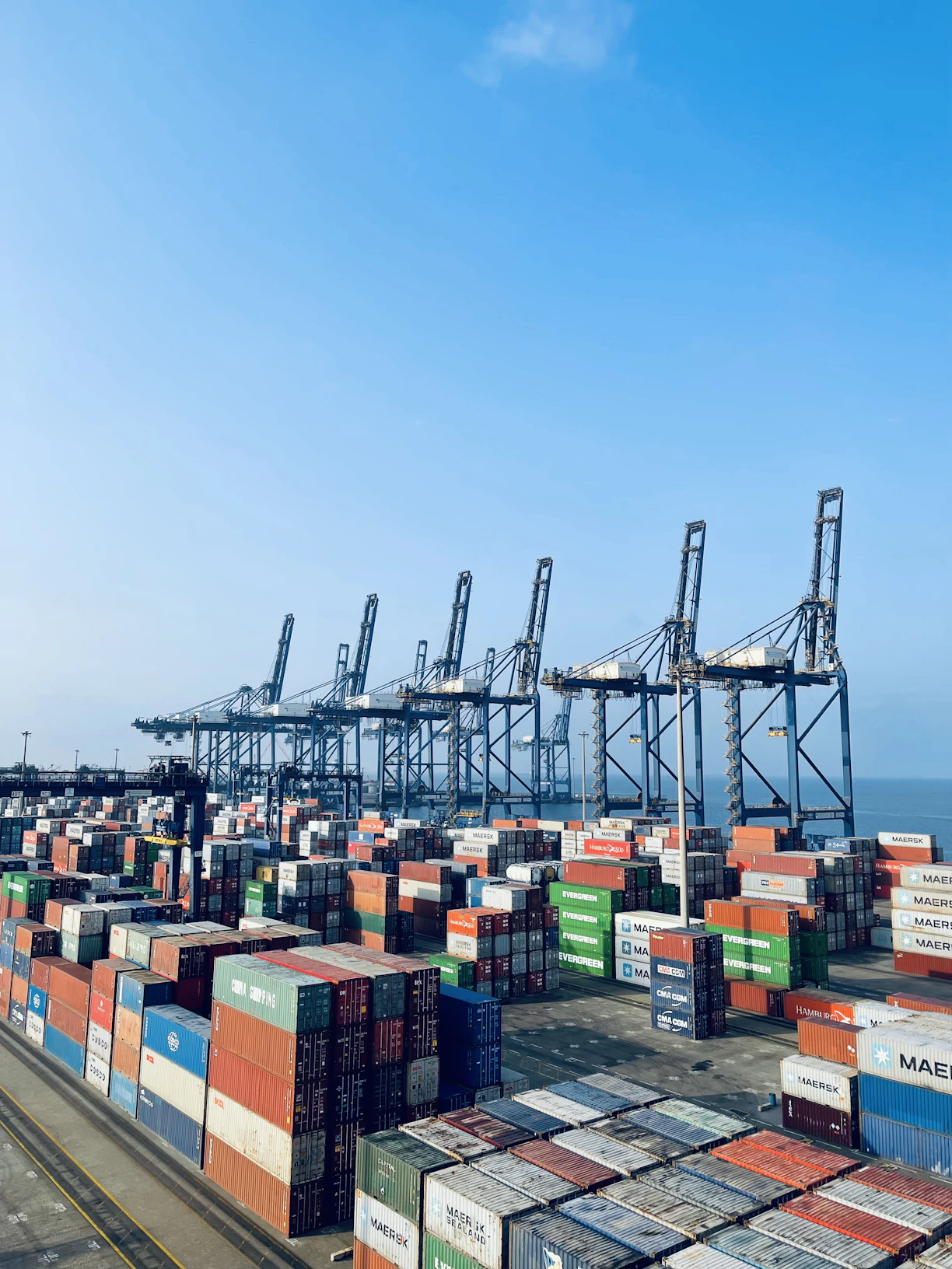 A busy port in Chattogram with cargo containers being loaded onto a ship under a clear blue sky.